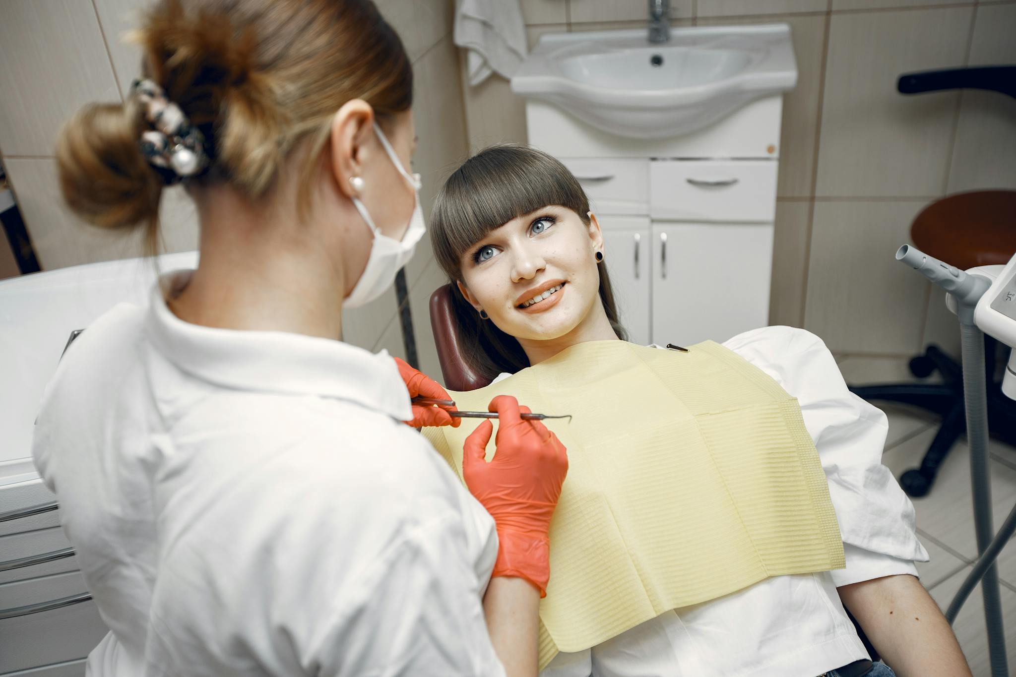 A dentist wearing a mask examines a patient in a contemporary dental office setting.