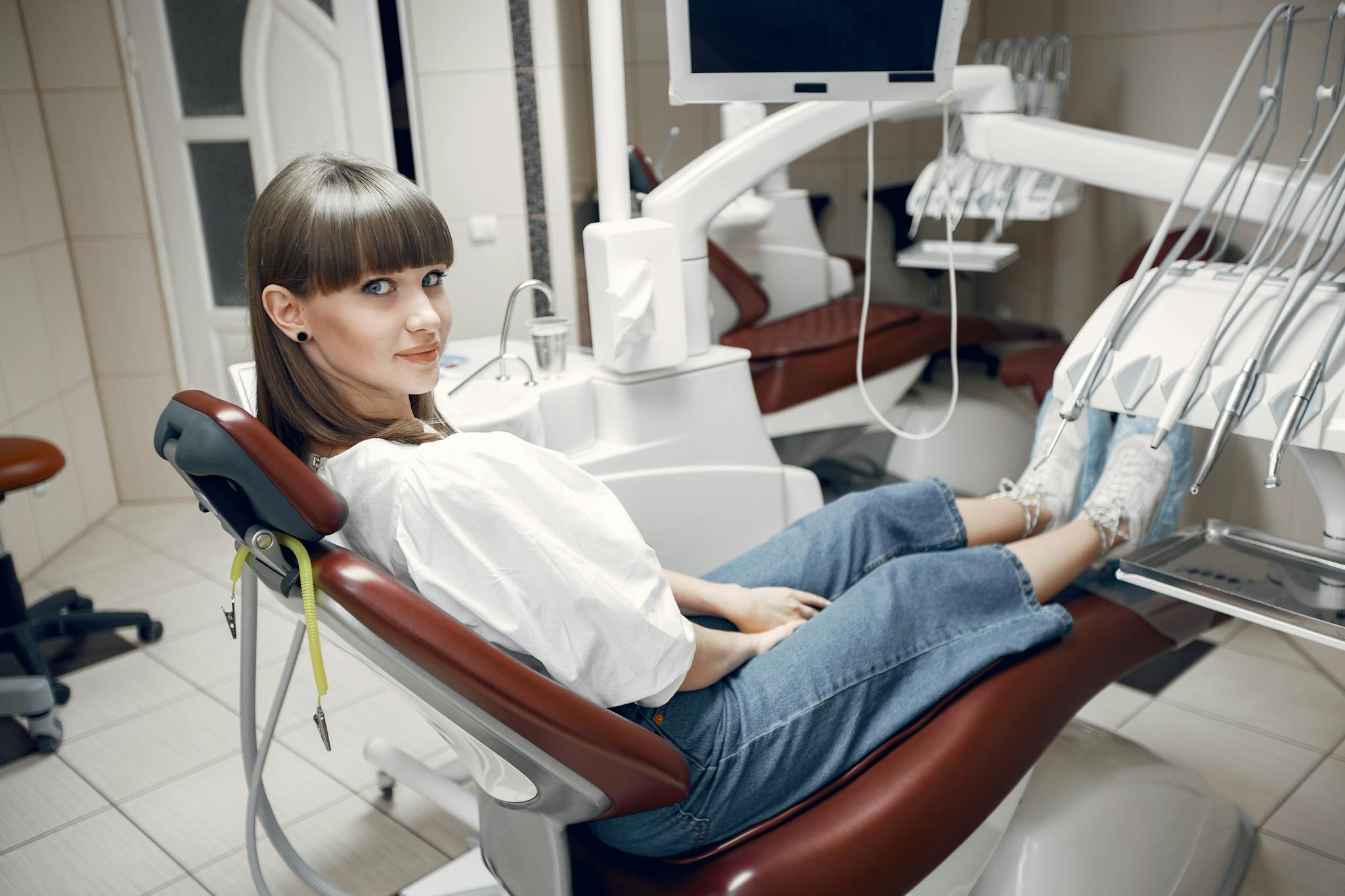 A young woman sitting comfortably in a modern dental clinic chair, smiling at the camera.