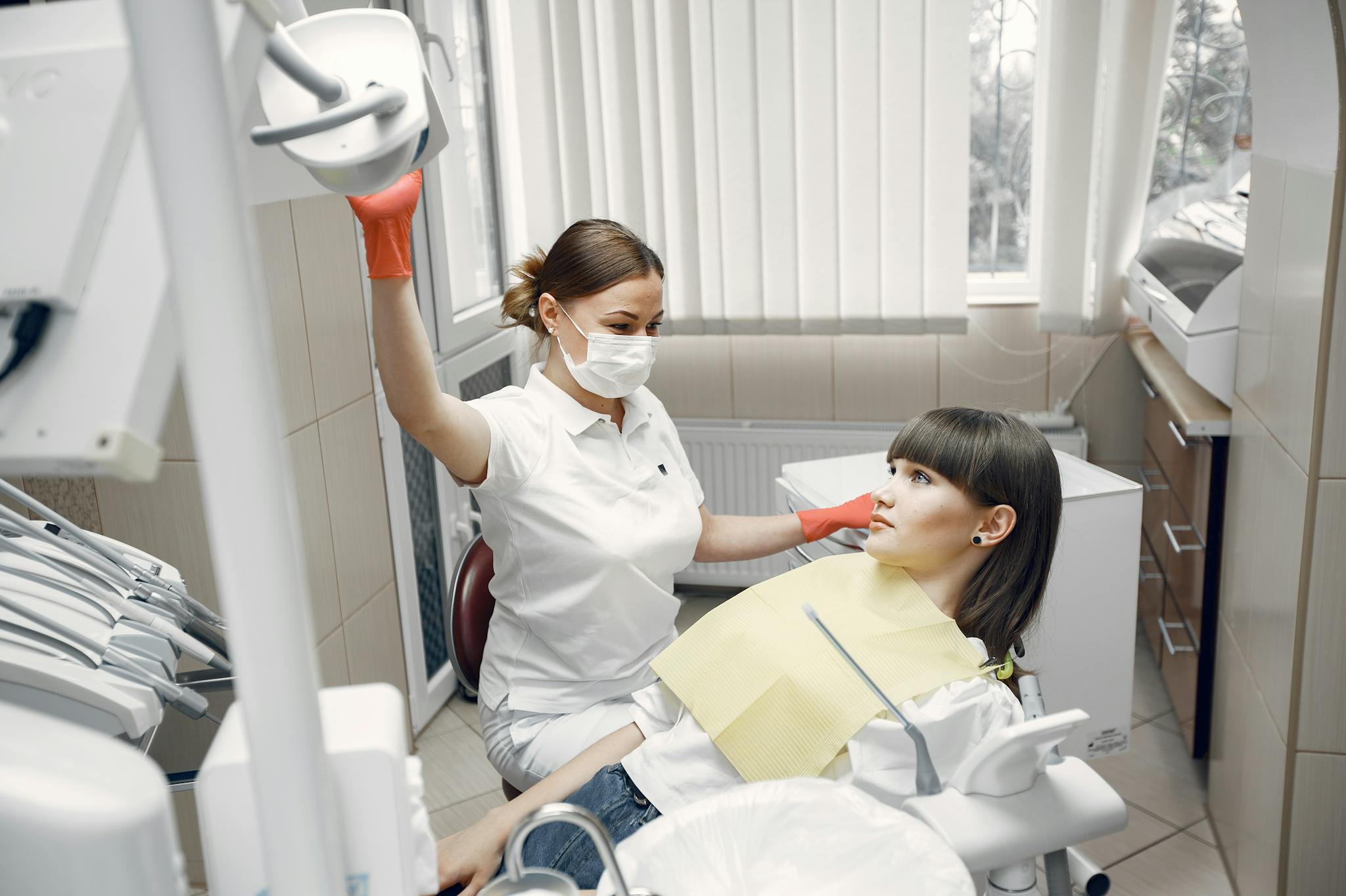 Dentist with face mask attending a woman in a dental chair, ensuring dental care.