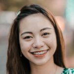 Close-up portrait of a smiling woman with braces, conveying joy and confidence outdoors.